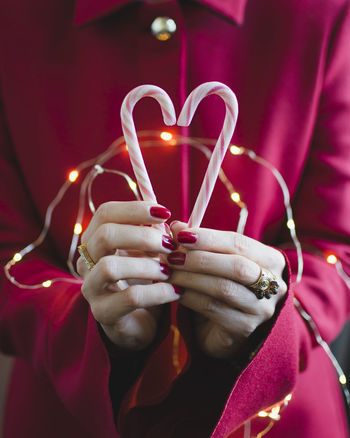 Midsection of woman with illuminated string lights holding candy canes during christmas