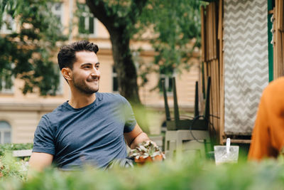 Smiling young man sitting with friend at restaurant in city