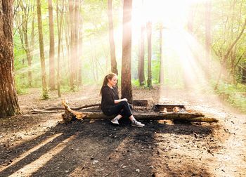 Full length of man sitting on tree trunk in forest