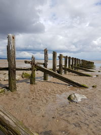 Wooden posts on beach against sky