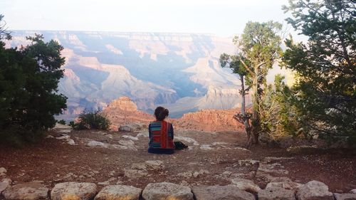 Rear view of mature woman sitting on cliff against grand canyon