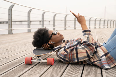 Thoughtful african woman with smartphone serious lying on skateboard on city quay urban space grumpy