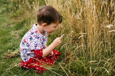 A young boy inspects some plants searching for bugs with a magnifying glass