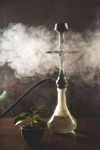 Close-up of hookah with smoke on table against black background