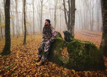 Rear view of man sitting on rock in forest