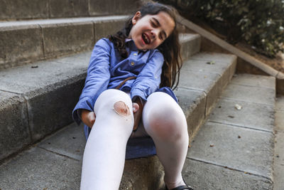 Girl with wounded leg sitting on steps