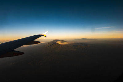 Airplane flying over landscape against sky during sunset