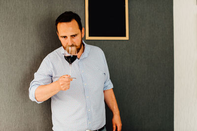 Man tasting and smelling red wine while standing at wall