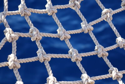 Close-up of rope tied on chain against blue sky