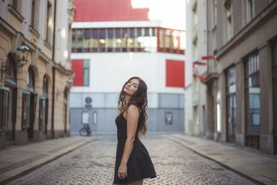 Portrait of beautiful woman standing on street amidst buildings in city