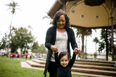 Grandmother holding granddaughter's hands while standing in park
