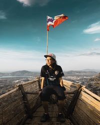 Man with umbrella standing by flag against sky