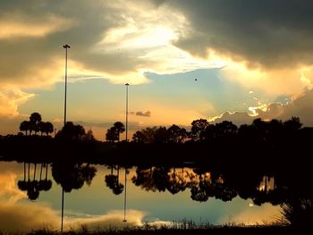 Silhouette trees by lake against sky during sunset