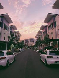 Cars on road by buildings against sky during sunset