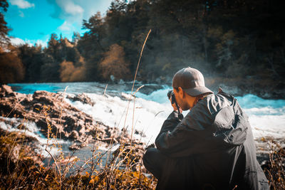 Rear view of man photographing river in forest