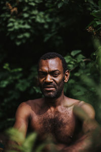 Portrait of shirtless man sitting against plants