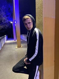 Portrait of young man standing against illuminated wall at night