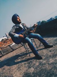 Full length of young man sitting against sky