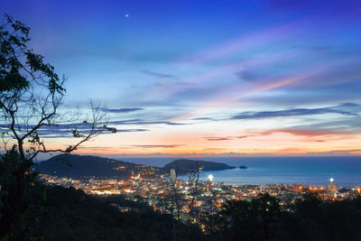 High angle view of illuminated city by sea against sky