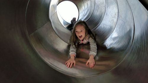 Cheerful girl sliding in tunnel slide at playground