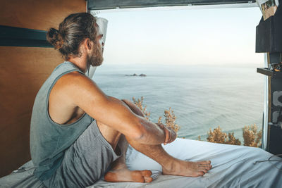 Man sitting in the back of a camper van looking at the sea
