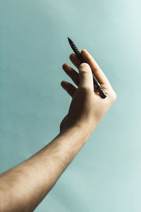 Cropped hand of man holding pen against colored background