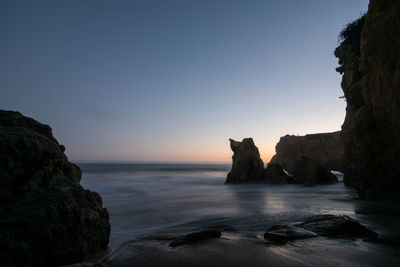 Rock formation on beach against sky during sunset