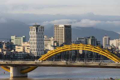 Bridge over river by buildings against sky in city