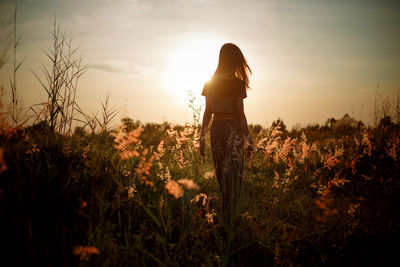 Woman standing on field against sky during sunset