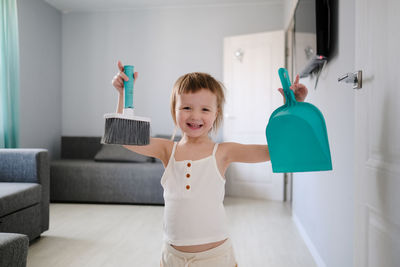 Cute european child with blue scoop for garbage and brush for sweeping floor helps to clean house