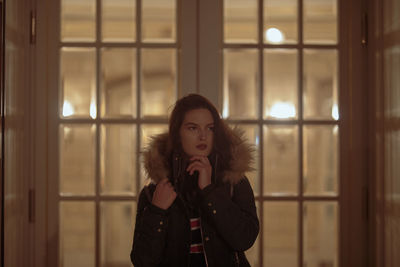 Thoughtful young woman standing against closed door at night