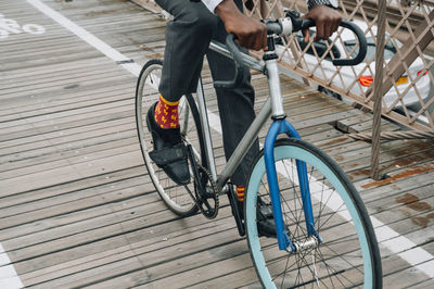 Cropped anonymous well dressed businessman cyclist in riding bike on wooden road among red metal structure with in new york city