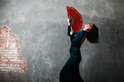 Side view of woman holding hand fan against wall