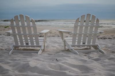 Empty chairs on beach against sky