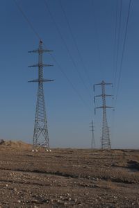 Low angle view of electricity pylons against clear blue sky