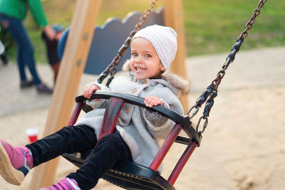 Cheerful cute girl sitting on swing at playground