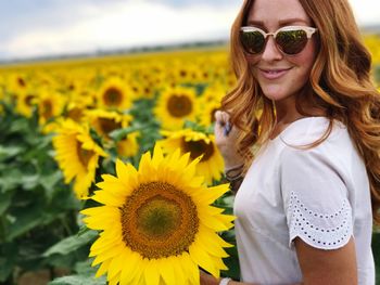 Portrait of smiling woman wearing sunglasses standing on sunflower filed
