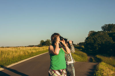 Woman photographing on road against clear sky