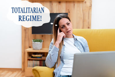 Young woman using smart phone while sitting on laptop