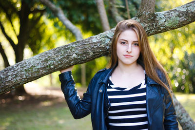 Portrait of woman standing against tree trunk at park