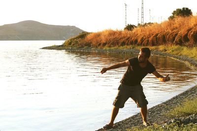 Full length of young man throwing stone in lake