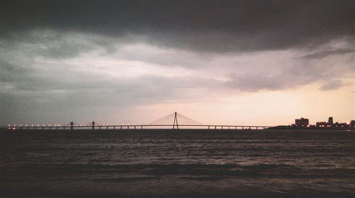 Suspension bridge over sea against cloudy sky