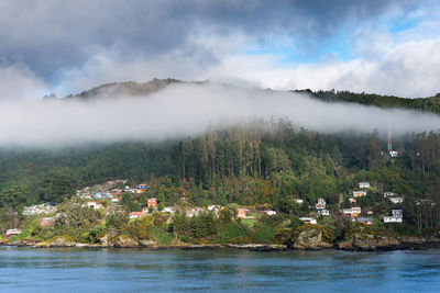 Townscape by river against mountains and cloudy sky