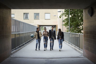 Full length of happy friends talking while walking on footbridge