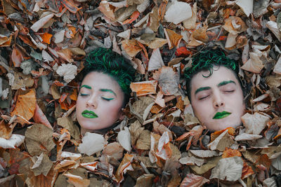 High angle view of friends with body paint lying amidst autumn leaves on field