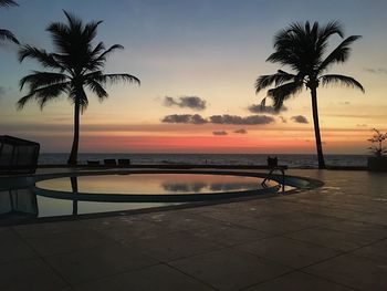 Silhouette palm tree by swimming pool against sky during sunset