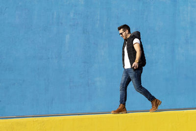 Bearded man with sunglasses walking on yellow wall