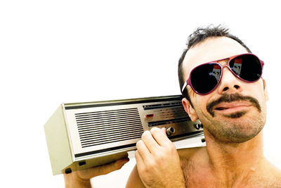 Portrait of man wearing sunglasses while holding radio against white background
