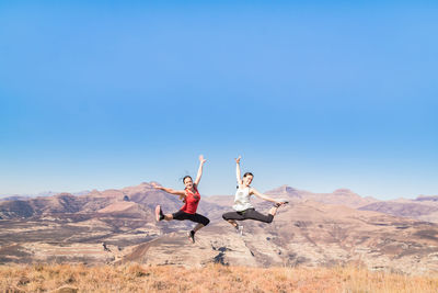 Happy friends with arms raised jumping on mountain against clear sky