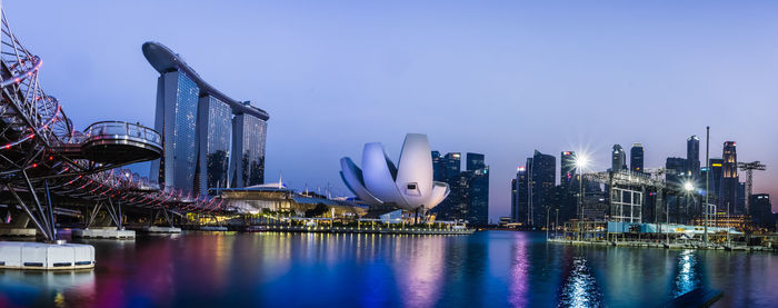 Illuminated city by river against sky